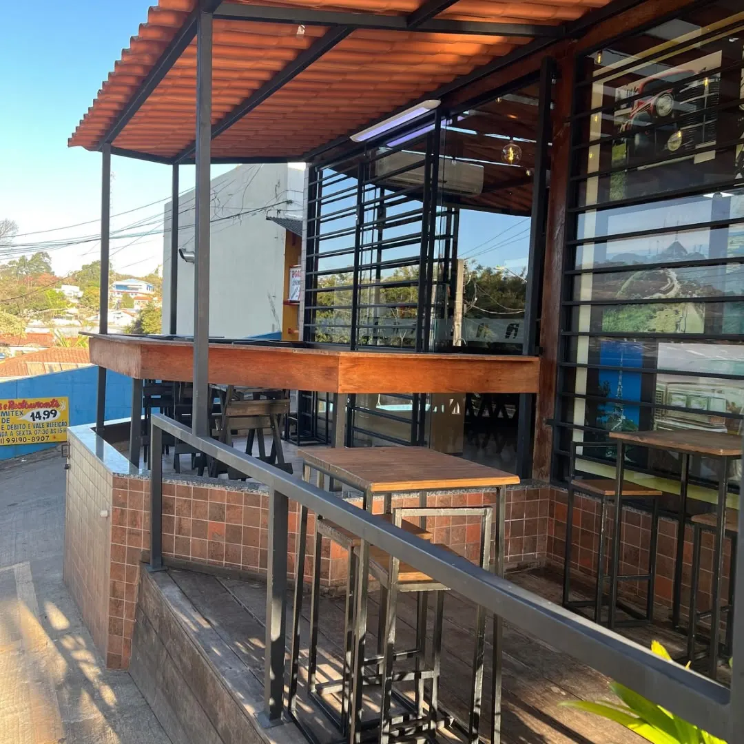 Área externa de cafeteria com balcões e mesas altas de madeira sob estrutura metálica