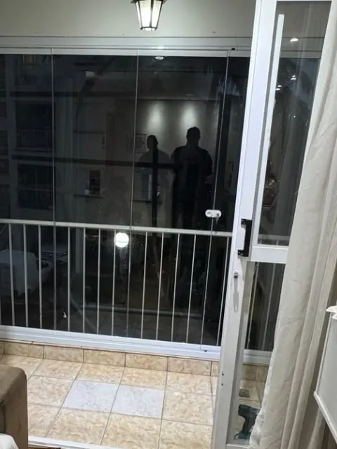 Sacada envidraçada vista de dentro do apartamento, com painéis de vidro e gradil