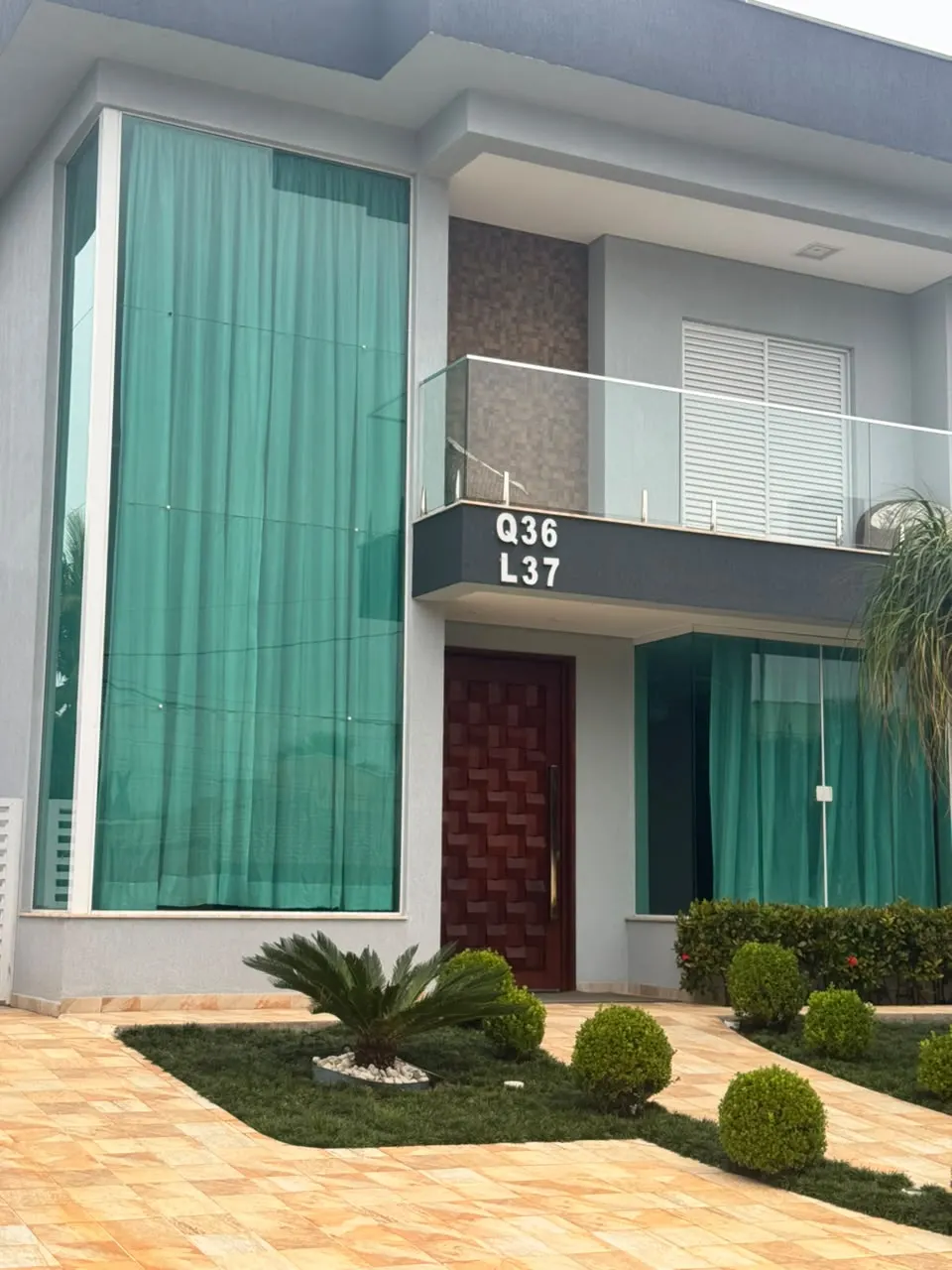 Fachada de casa com panos de vidro verde de pé-direito duplo e guarda-corpo de vidro na sacada