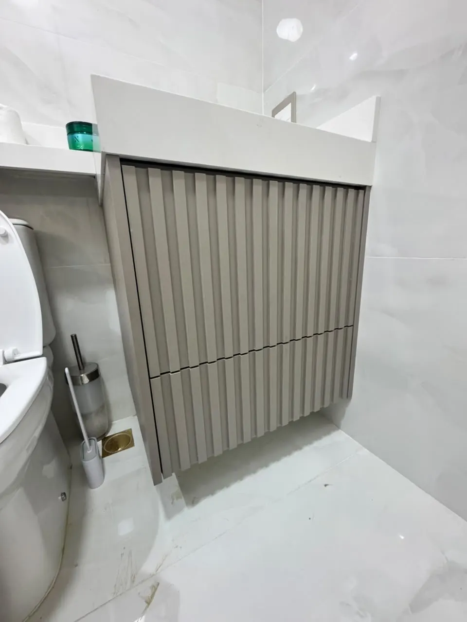 Detalhe de gabinete ripado sob bancada branca de banheiro