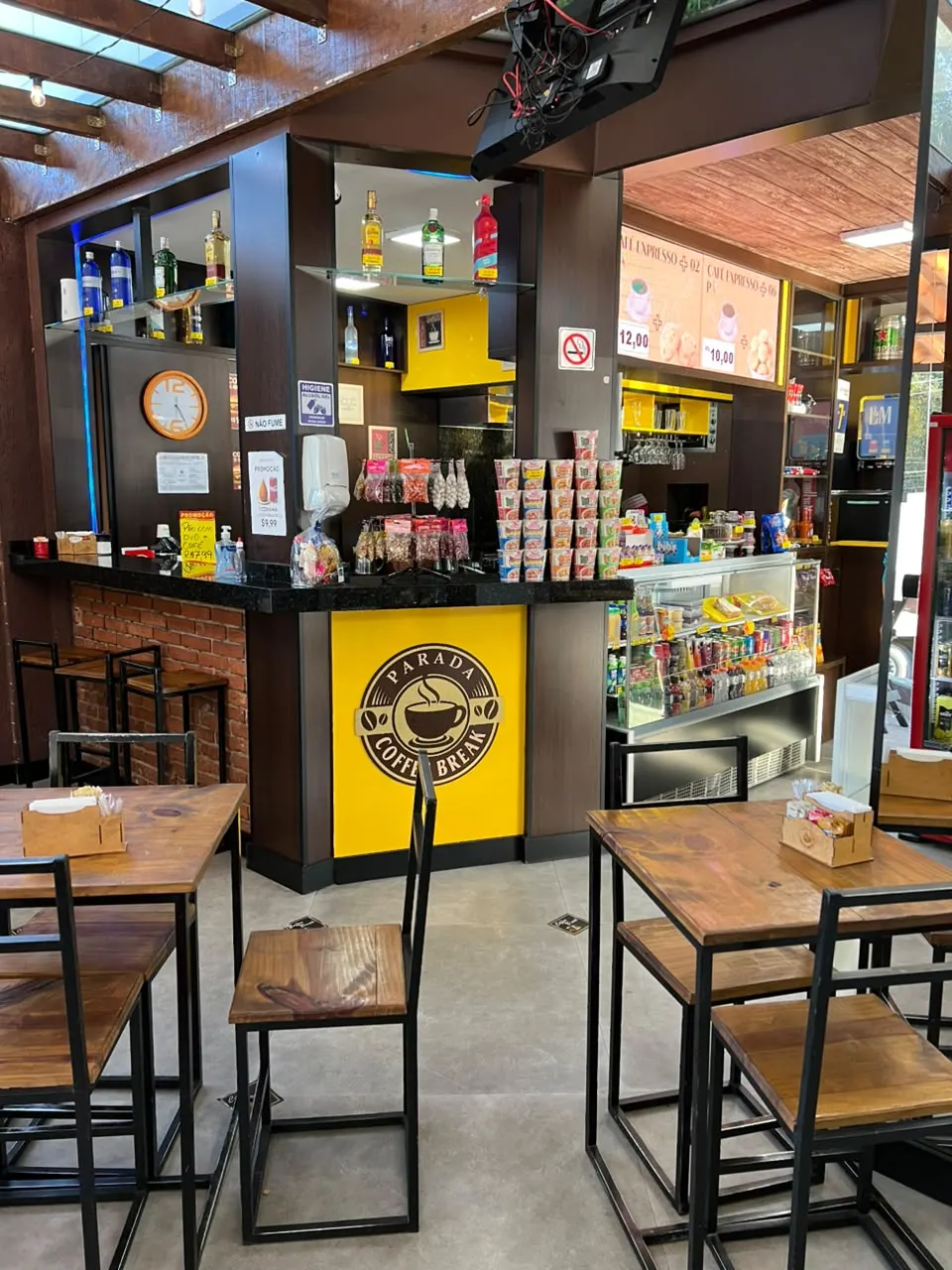 Cafeteria com balcão, prateleiras e mesas altas em madeira e metal