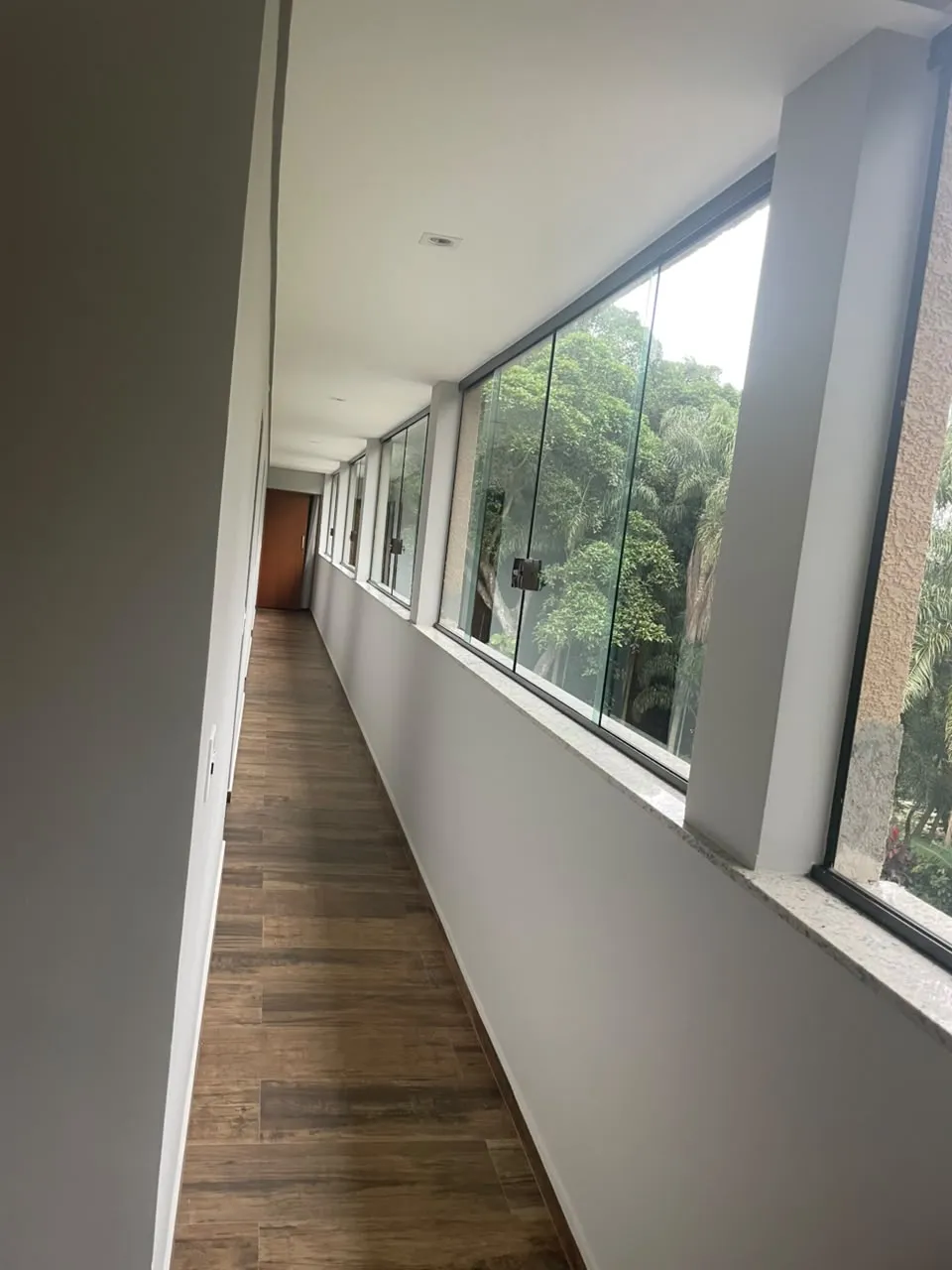 Corredor com sequência de janelas de vidro e piso de madeira