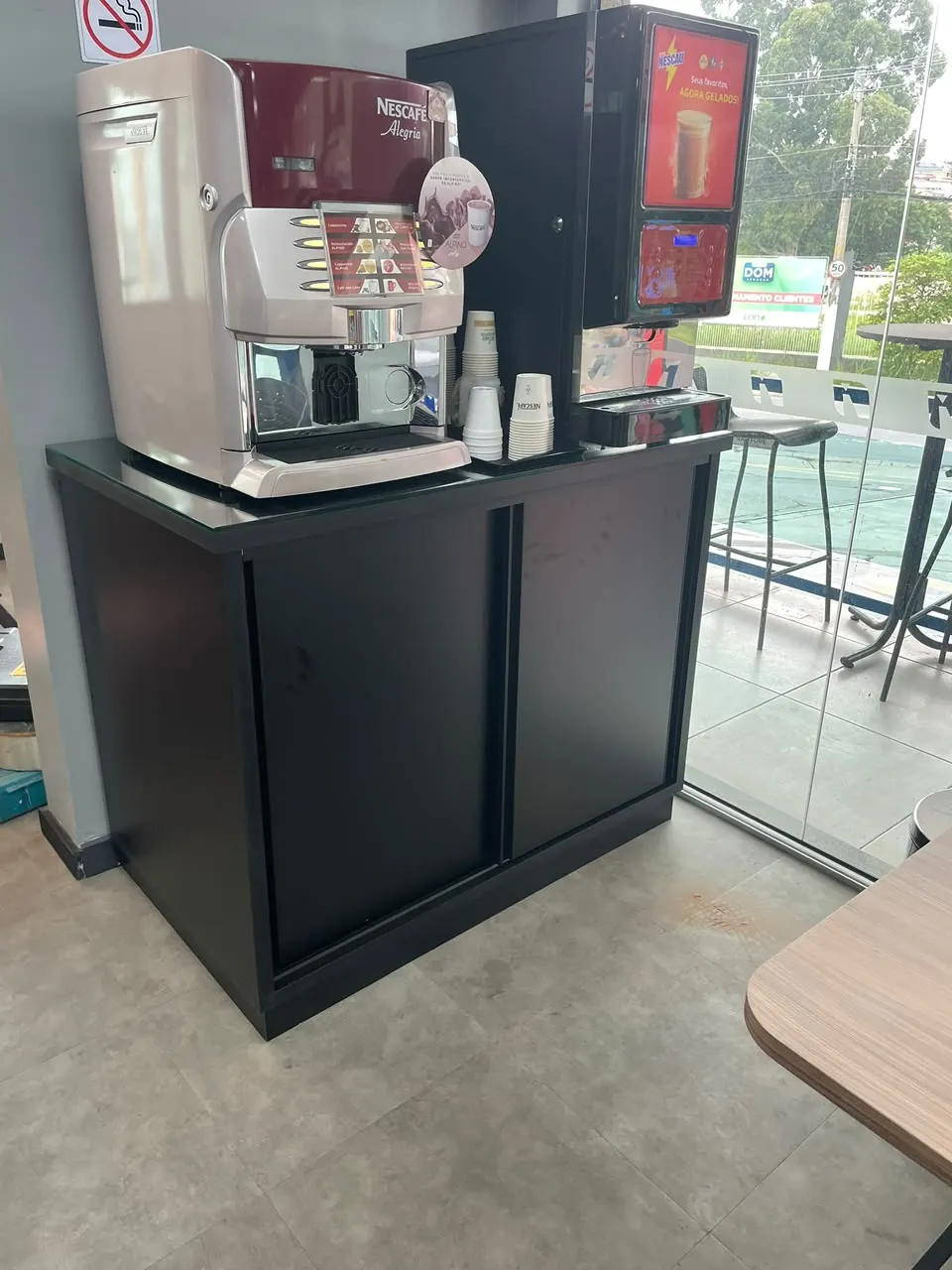 Armário baixo preto com portas de correr, apoiando máquinas de café