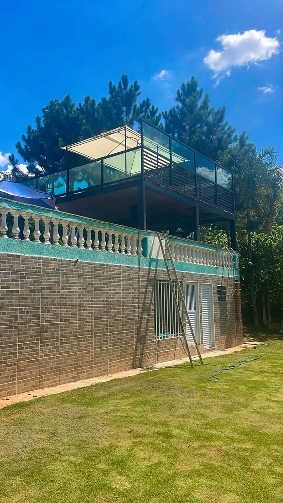Deck elevado com guarda-corpo de vidro visto do gramado, sob céu azul